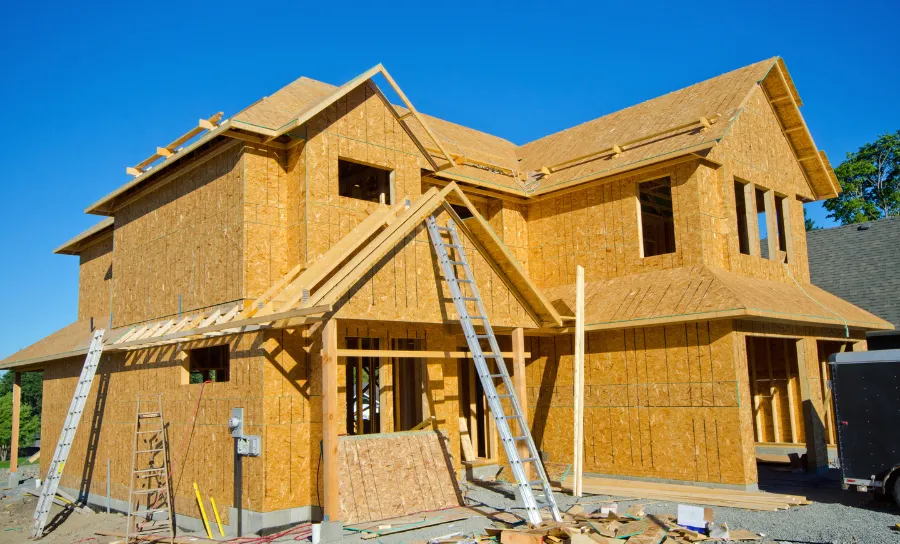 Residential home under construction showing full wood framing structure and roof trusses before exterior finishes